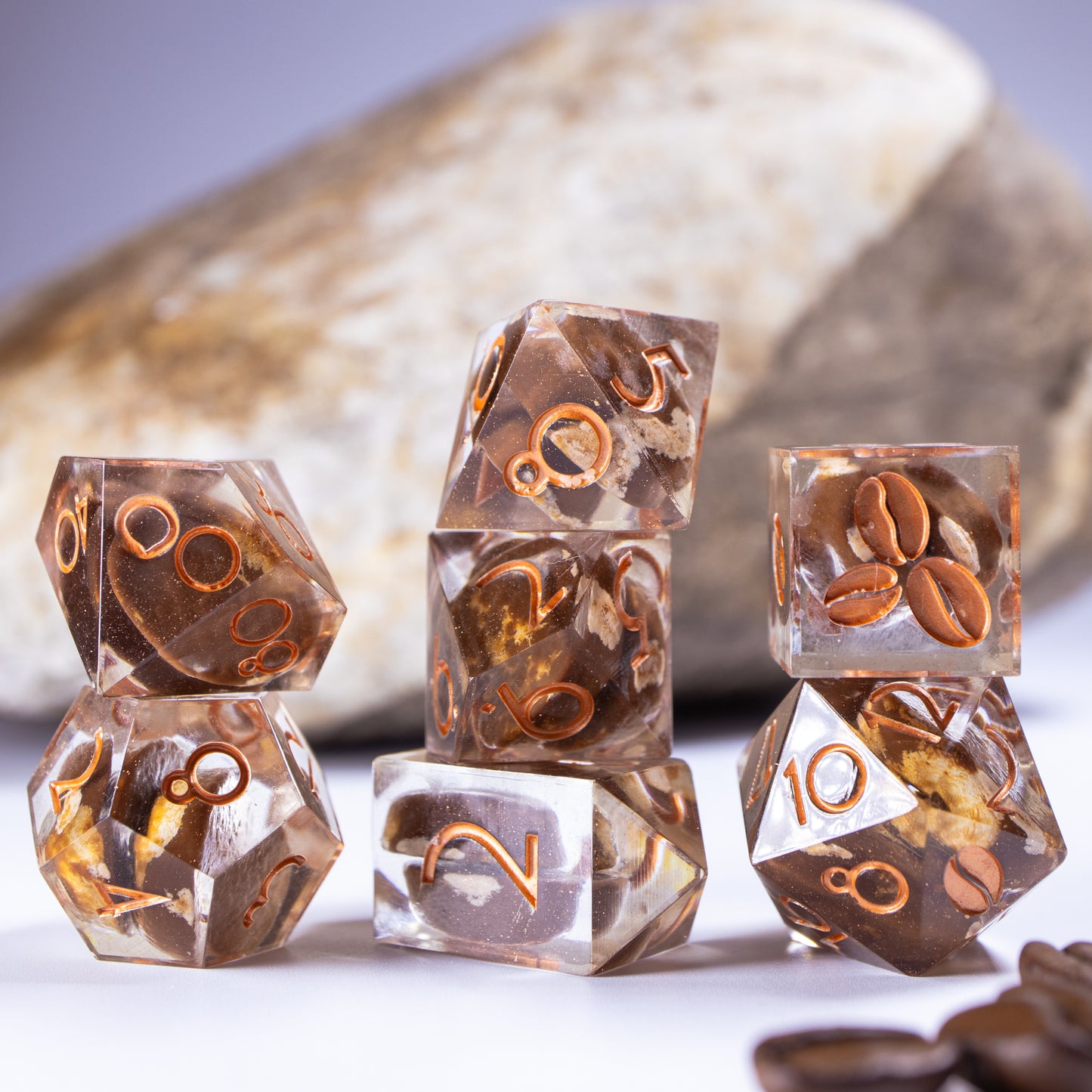 Three towers of stacked coffee themed dice with added background elements, such as an out of focus rock for added texture and decorative coffee beans.