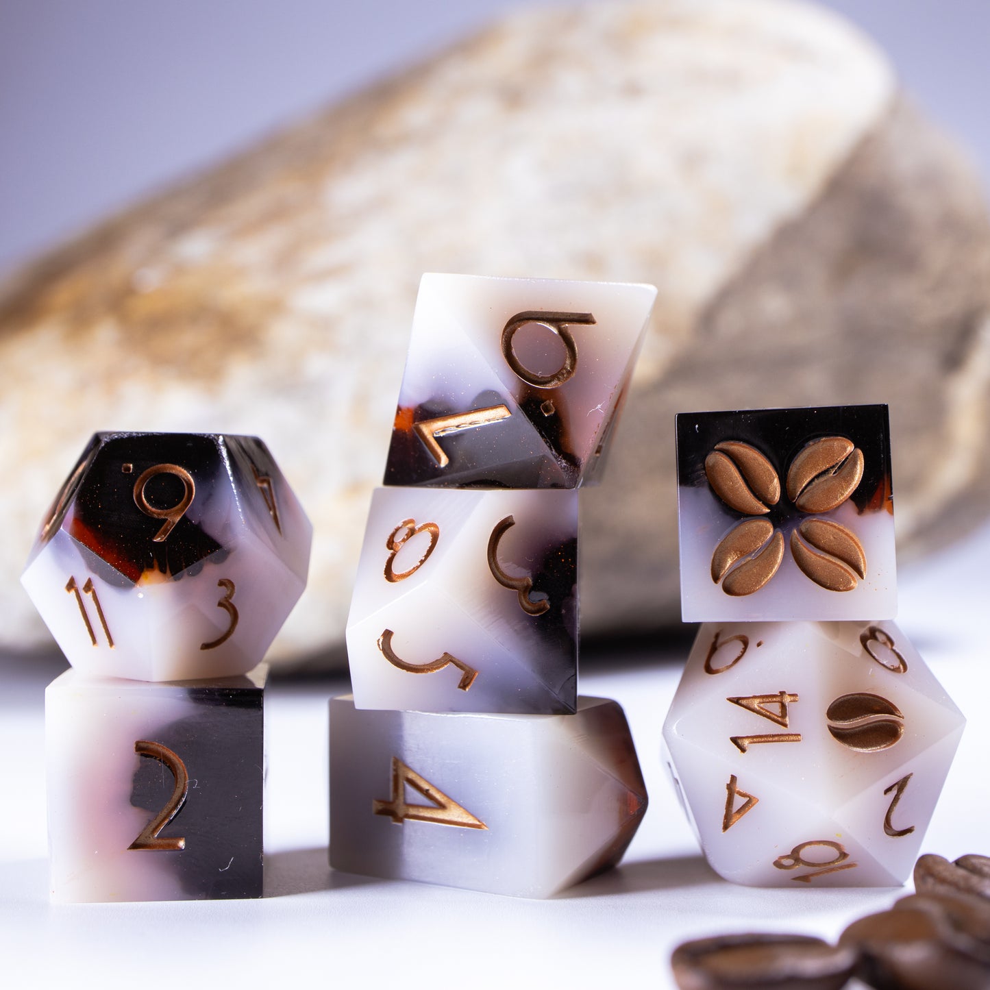Three towers of stacked coffee themed dice with added background elements, such as an out of focus rock for added texture and decorative coffee beans.