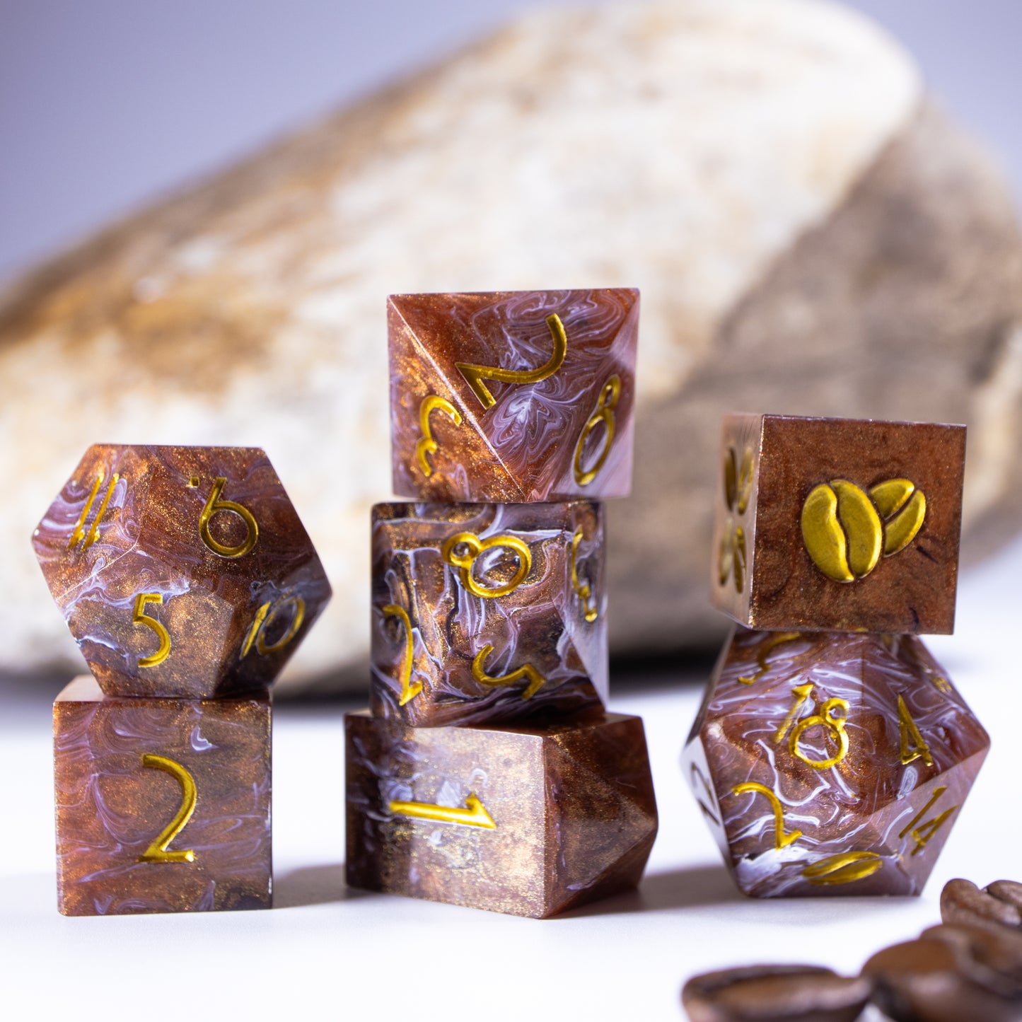 Three towers of stacked coffee themed dice with added background elements, such as an out of focus rock for added texture and decorative coffee beans.