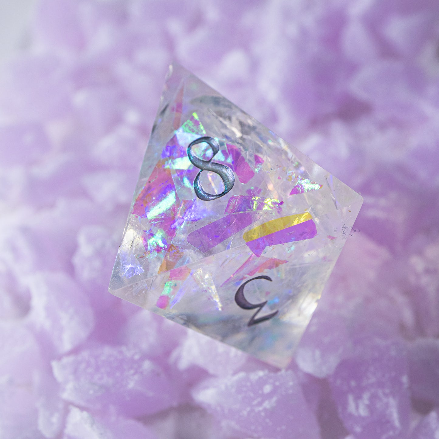 An eight-sided die, nestled gently on a pile of decorative lilac wax shards.