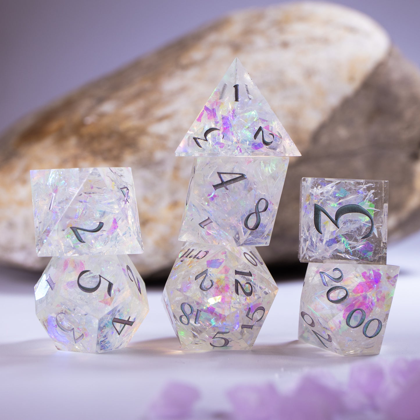 Three towers of stacked polyhedral dice with added background elements, such as an out of focus rock for added texture and tiny decorative wax shards.