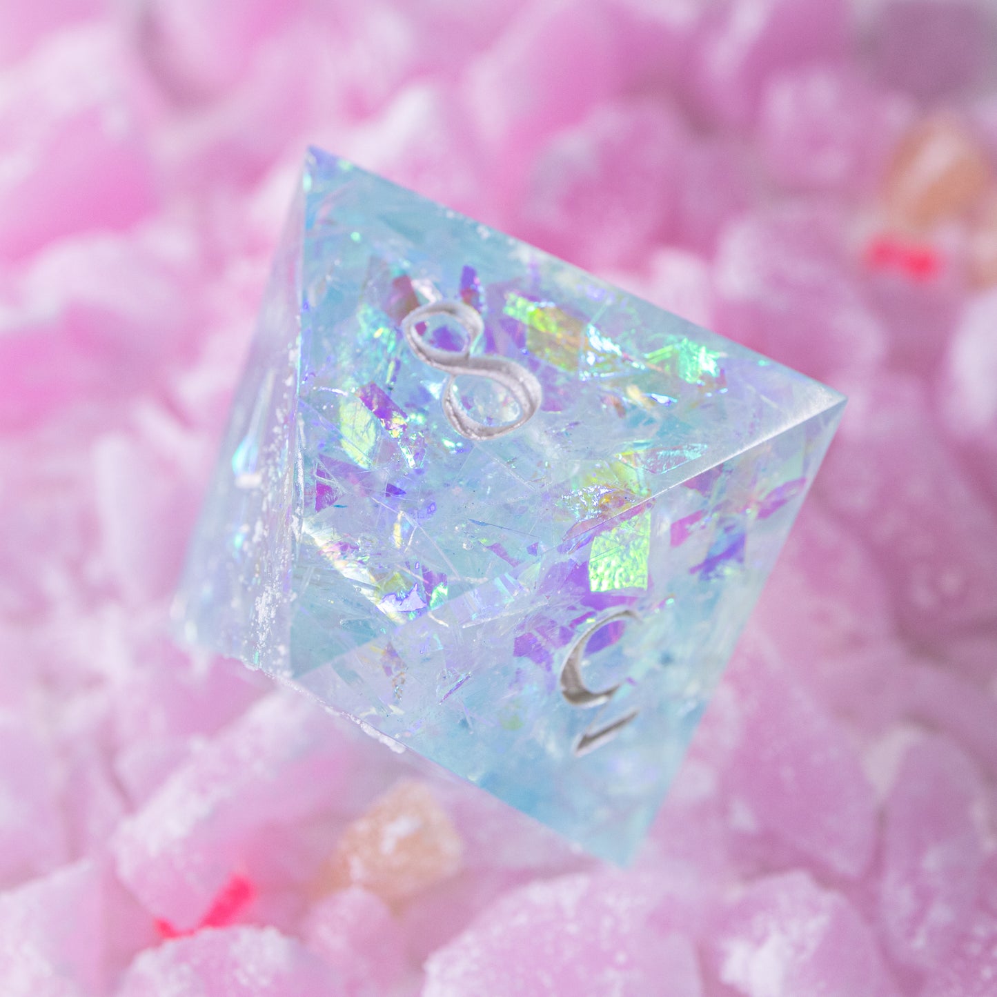 An eight-sided die, nestled gently on a pile of decorative pink wax shards.