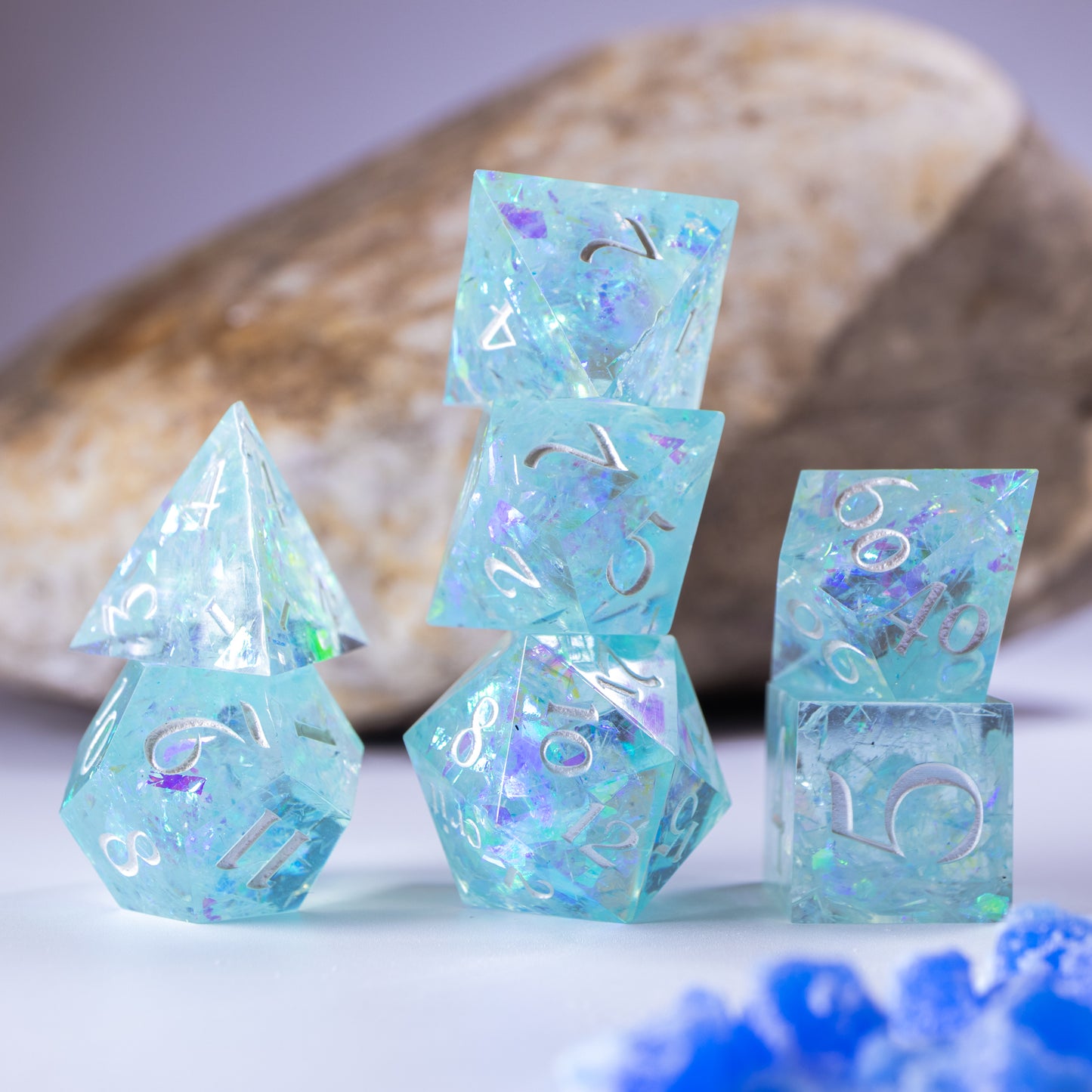 Three towers of stacked polyhedral dice with added background elements, such as an out of focus rock for added texture and tiny decorative wax shards.