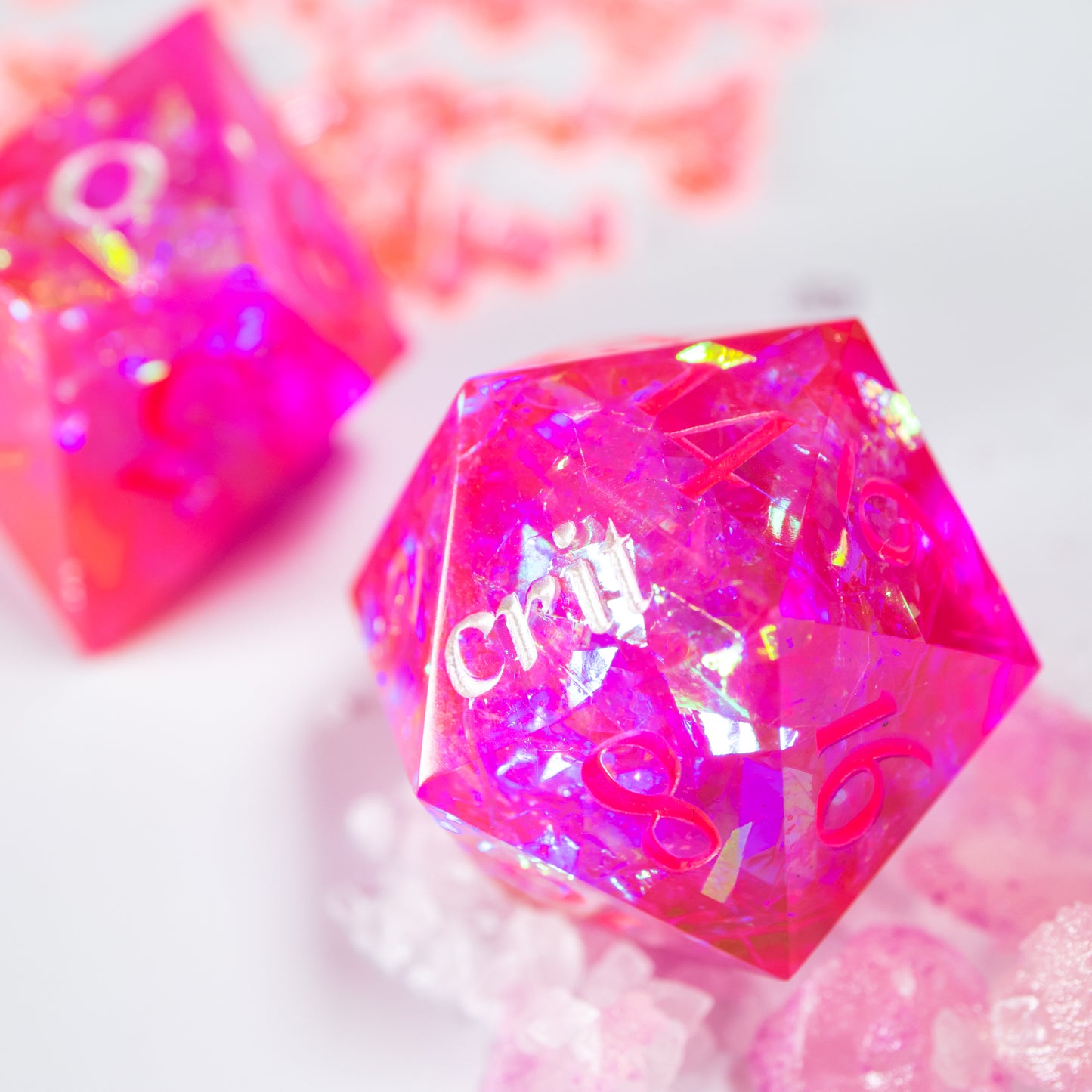 A close-up of an almost blaring neon-pink twenty sided die. Behind it lies a ten sided die, among a scattering of tiny decorative pink shards.
