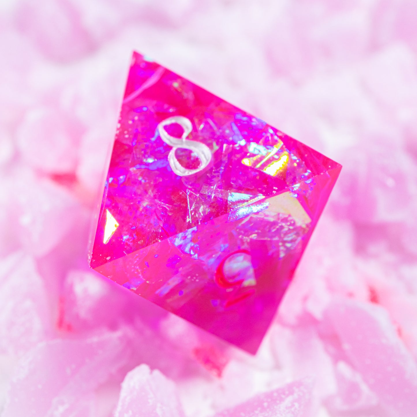 An eight-sided die, nestled gently on a pile of decorative pink wax shards.