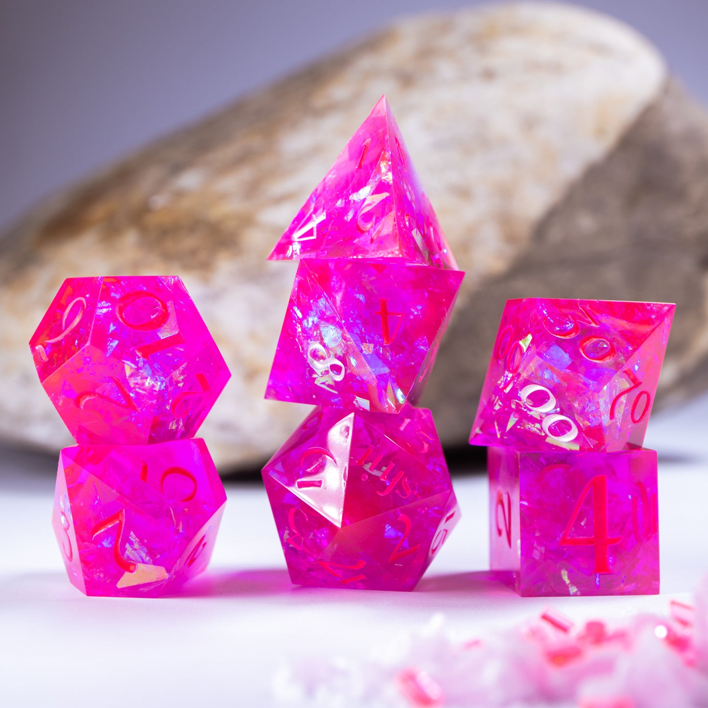 Three towers of stacked polyhedral dice with added background elements, such as an out of focus rock for added texture and tiny decorative wax shards.