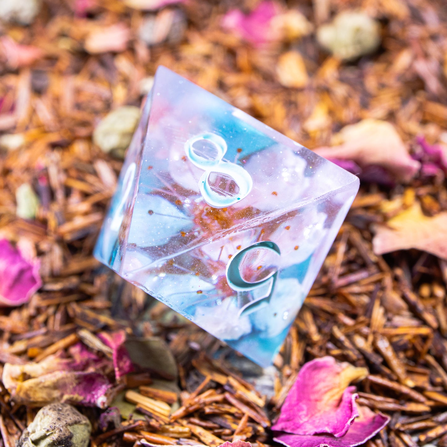 An eight-sided die, nestled gently on a pile of decorative leaves and petals.