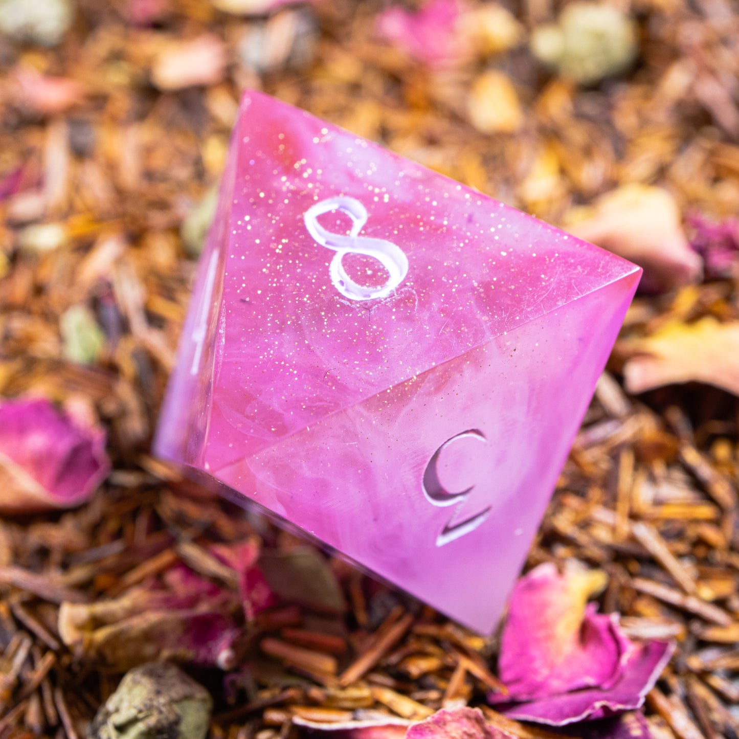 An eight-sided die, nestled gently on a pile of decorative leaves and petals.