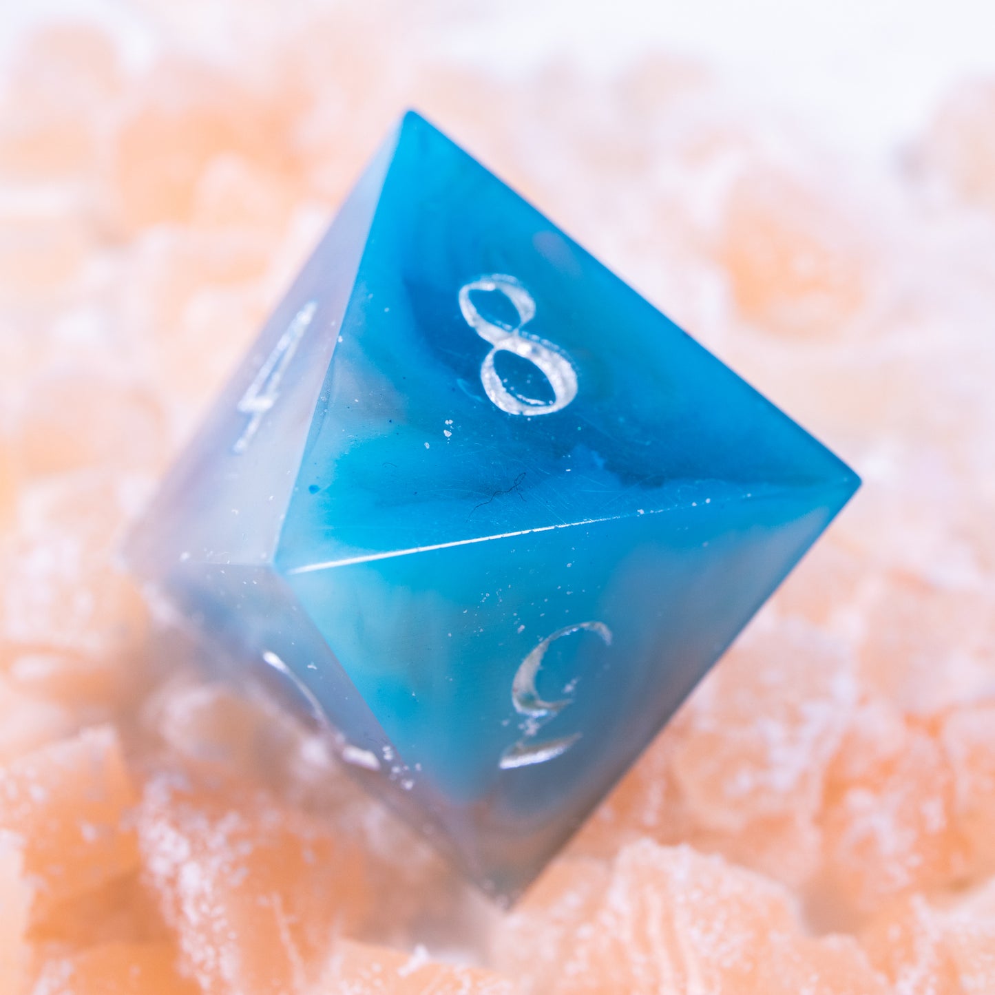 An eight-sided die, nestled gently on a pile of decorative orange wax shards.