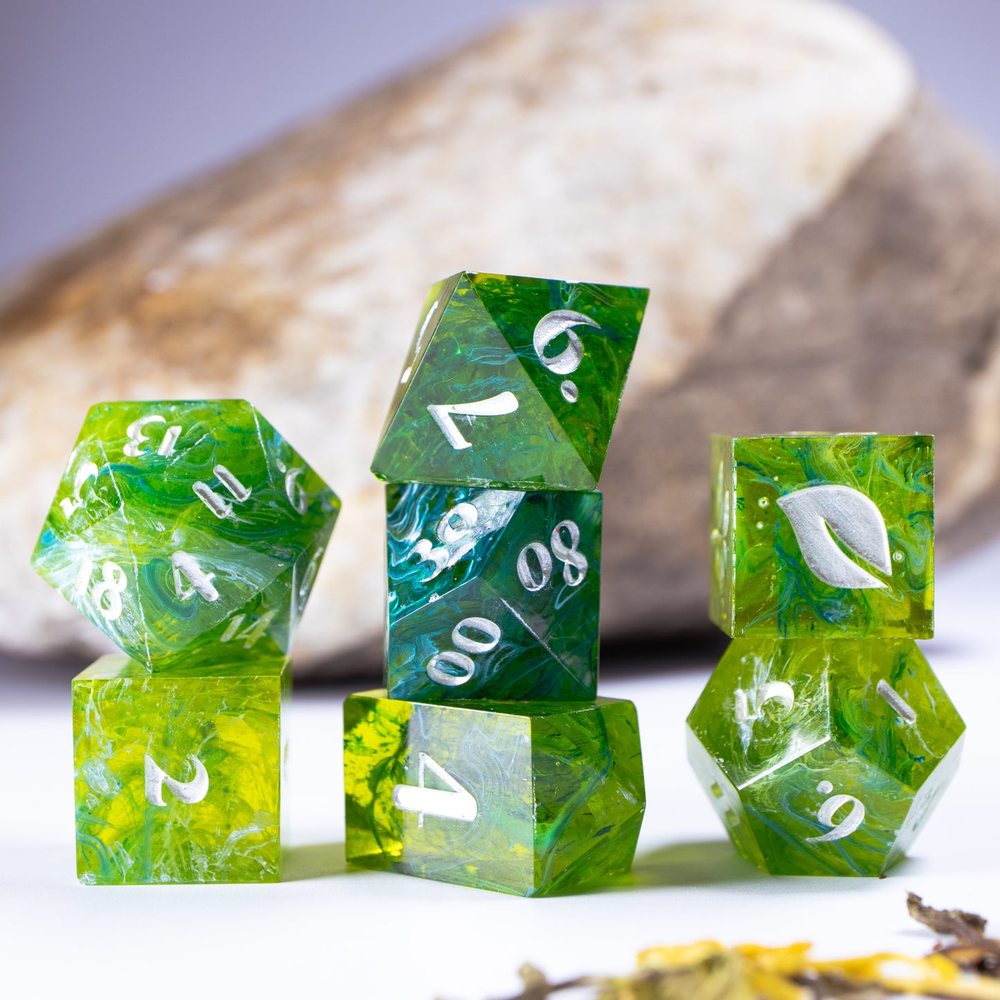 Three towers of stacked coffee themed dice with added background elements, such as an out of focus rock for added texture and decorative tea leaves.