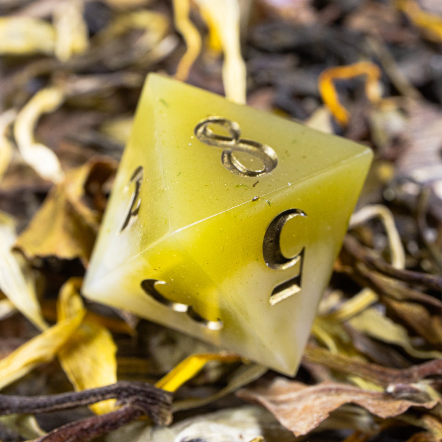 An eight-sided die, nestled gently on a pile of decorative tea leaves.