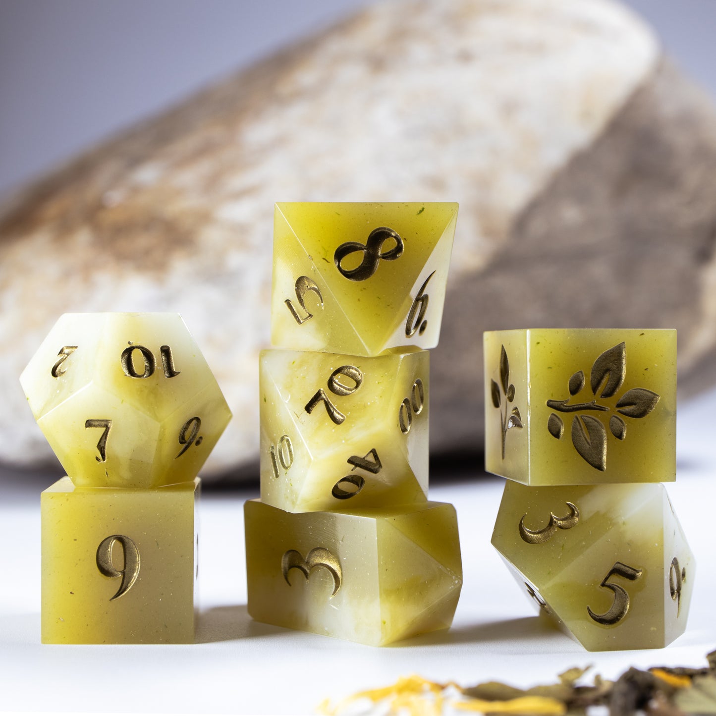 Three towers of stacked coffee themed dice with added background elements, such as an out of focus rock for added texture and decorative tea leaves.
